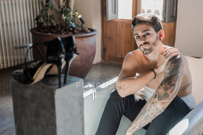 Cool hombre provocativo sin camisa con el brazo tatuado relajándose solo en la bañera - foto de stock