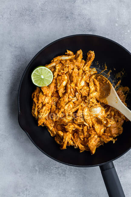 Vista dall'alto del gustoso curry di pollo tradizionale piccante con lime in padella nera con cucchiaio di legno su sfondo grigio pietra — Foto stock