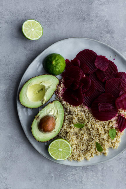 Top view of plate with cooked quinoa and sliced beetroot with avocado and lime on grey background — Stock Photo
