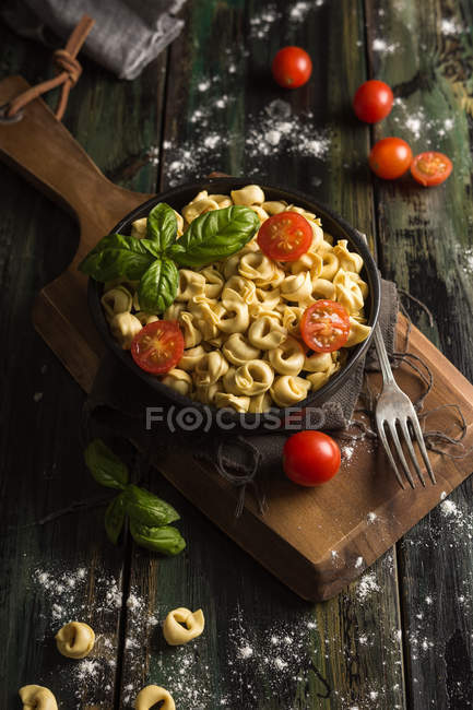 From above of full black plate with delicious homemade ravioli with cut cherry tomatoes and fresh basil on wooden cutting board placed on wooden plank table — Stock Photo