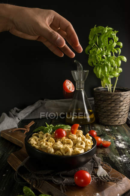 Hombre añadiendo tomates al tazón con ravioles - foto de stock