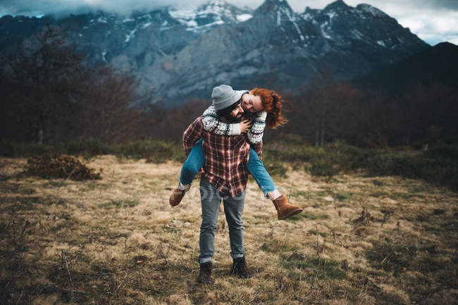Bella coppia abbracciare e trascorrere del tempo insieme a cavalluccio e viaggiare in prato con erba secca vicino a montagne in giornata nuvolosa — Foto stock