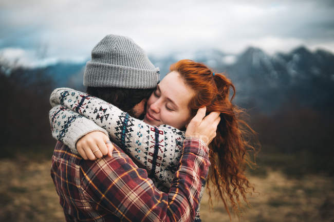 Vista lateral do casal terno abraço e ligação com os olhos fechados no dia frio nas montanhas — Fotografia de Stock