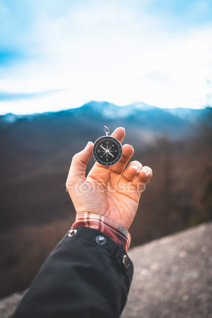 Crop person finding direction and holding compass in stretched hand in mountains — Stock Photo