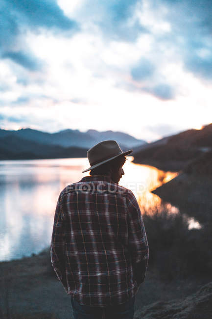 Вид ззаду мандрівника в куртці в капелюсі і сорочці на кам'янистих горах під час заходу сонця — стокове фото