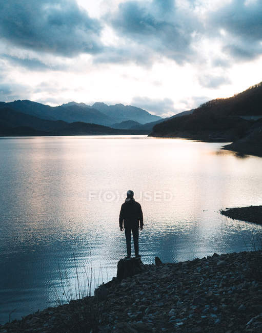 Back view of traveler in jacket in hat and shirt on stony mountains during sunset — Stock Photo