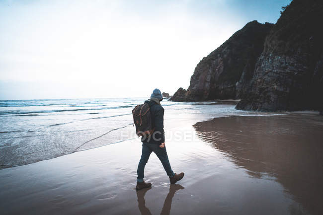 Вид ззаду анонімного мандрівника в куртці з рюкзаком з видом на море в оточенні гори — стокове фото