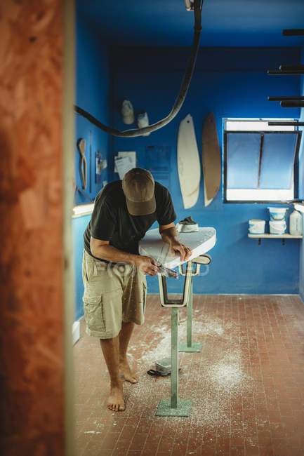 Woodworker diligently skinning surfboard in workshop — Stock Photo