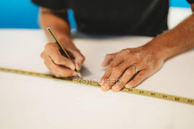 Cropped image of Workman with measuring tape making surf board — Stock Photo