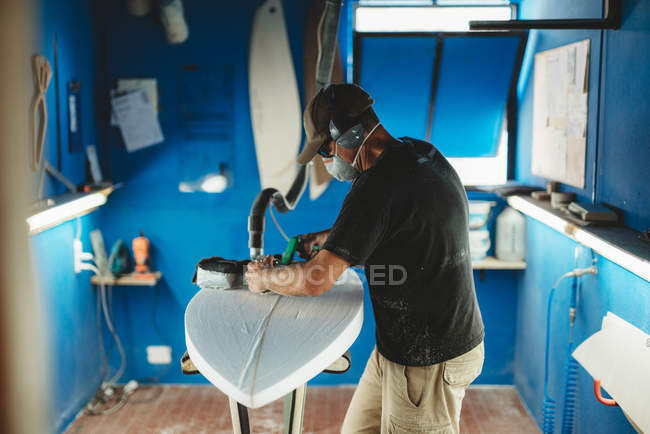 Працівник в захисній масці коригування деталей дошки для серфінгу в майстерні — стокове фото
