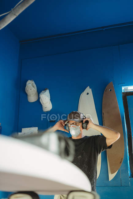 Trabalhador em máscara protetora ajustando detalhes prancha de surf na oficina — Fotografia de Stock