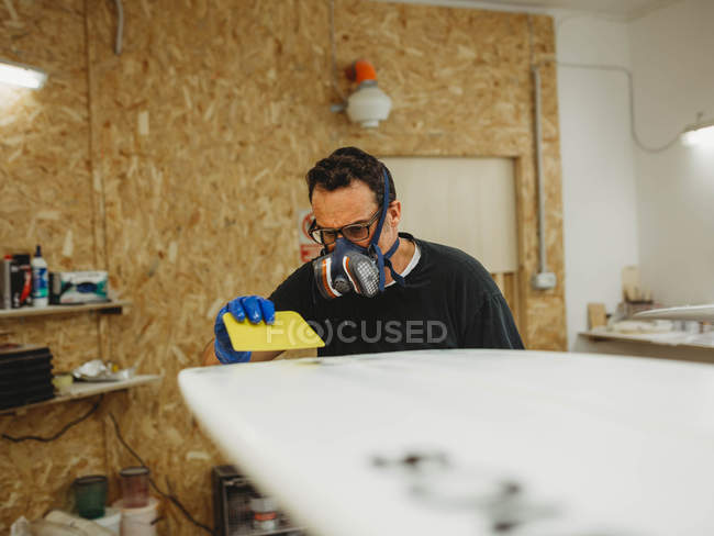 Дорослі майстри в захисній масці та рукавичках полірують білий серфінг під час роботи в маленькій майстерні. — стокове фото