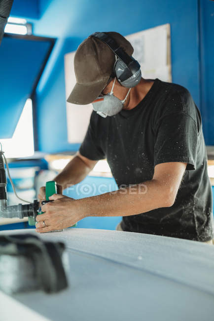 Trabajador en máscara protectora ajustando detalles tabla de surf en taller - foto de stock
