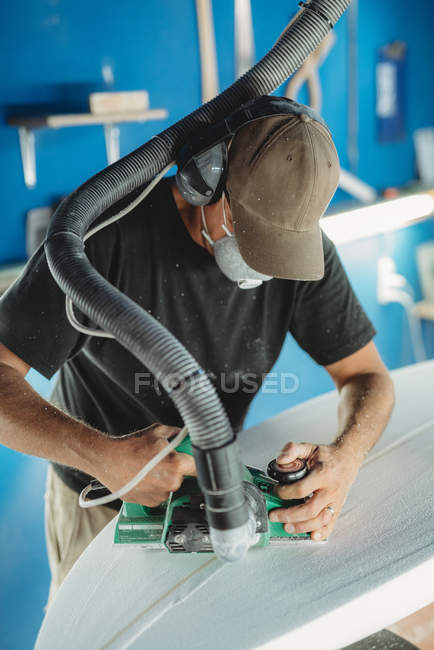 Trabalhador em máscara protetora ajustando detalhes prancha de surf na oficina — Fotografia de Stock