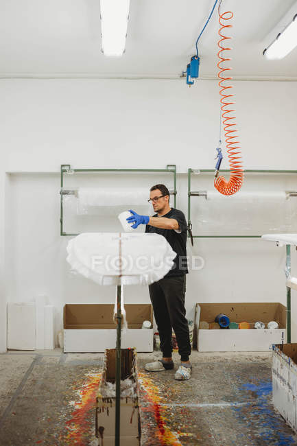 Handyman painting surf board in workshop — Stock Photo