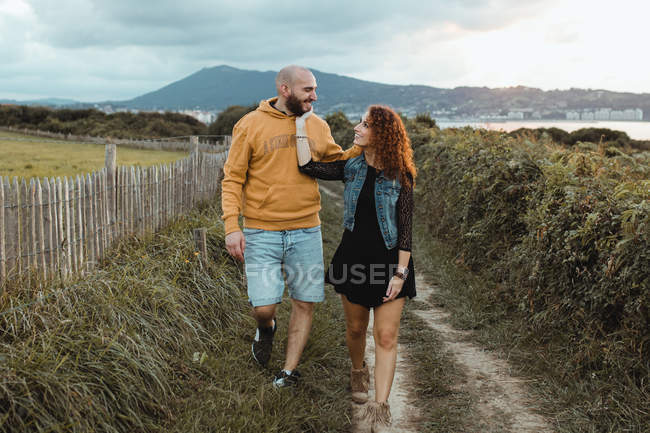 Mujer tierna cariñosa tocando la barbilla del hombre amado mientras caminan juntos en la pasarela a lo largo de la granja verde - foto de stock