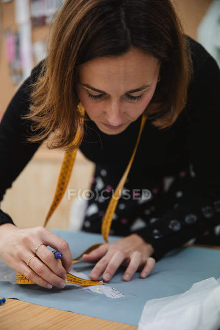 Donna adulta che usa il nastro per misurare la parte dell'indumento sul tavolo durante il lavoro nel laboratorio di sartoria professionale — Foto stock