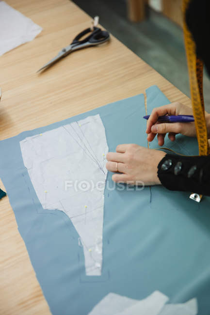 Взрослая женщина, использующая ленту для измерения части одежды на столе во время работы в профессиональной швейной мастерской — стоковое фото