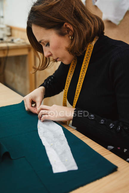 Schneiderin näht in professioneller Werkstatt mit Nadel und Faden maßgeschneiderte Kleidung über den Tisch — Stockfoto
