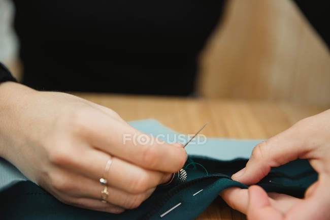 Fechar a costureira usando agulha e linha para costurar roupas personalizadas sobre a mesa na oficina profissional — Fotografia de Stock