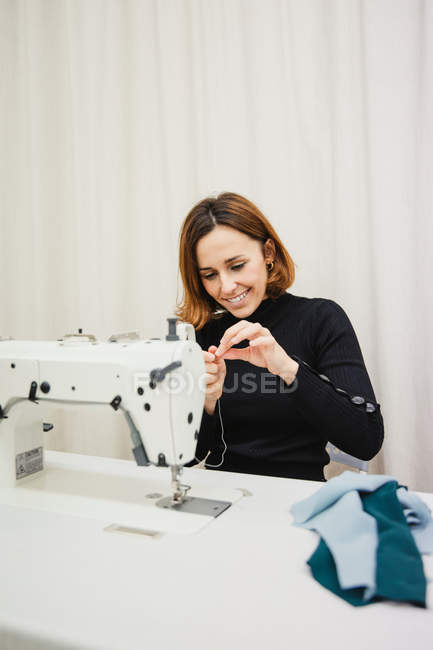 Femme adulte assise à table et faisant partie de vêtement sur la machine à coudre tout en travaillant dans un studio professionnel — Photo de stock