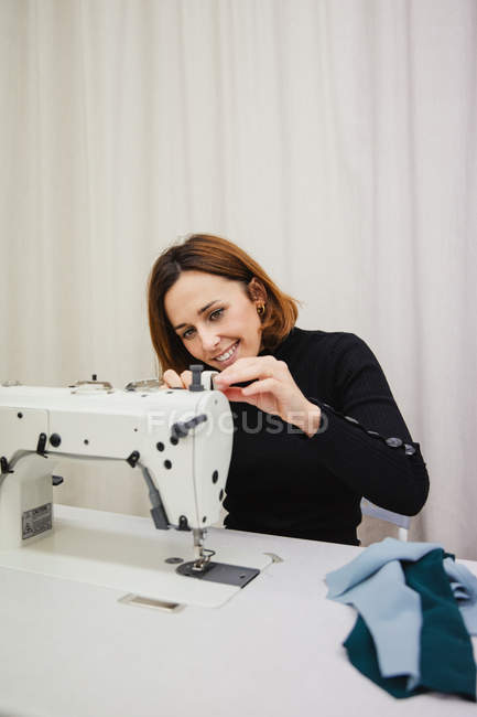 Erwachsene Frau sitzt am Tisch und macht Kleidungsstück Teil auf Nähmaschine, während sie im professionellen Studio arbeitet — Stockfoto
