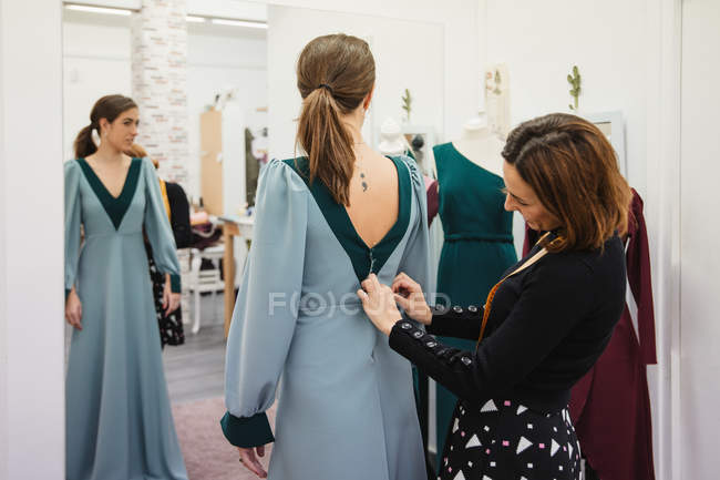 Schneiderin montiert maßgeschneidertes Kleid auf dem Rücken der Kundin, während sie in der professionellen Werkstatt arbeitet — Stockfoto