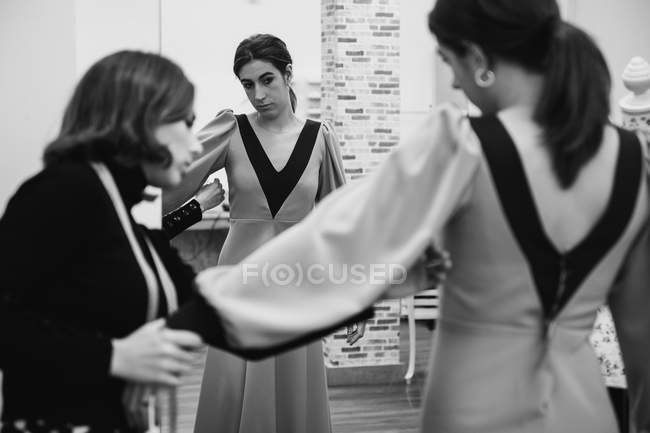 Dressmaker fitting custom gown on back of female client while working in professional workshop — Stock Photo