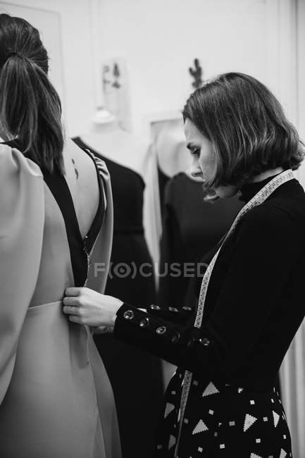 Schneiderin montiert maßgeschneidertes Kleid auf dem Rücken der Kundin, während sie in der professionellen Werkstatt arbeitet — Stockfoto