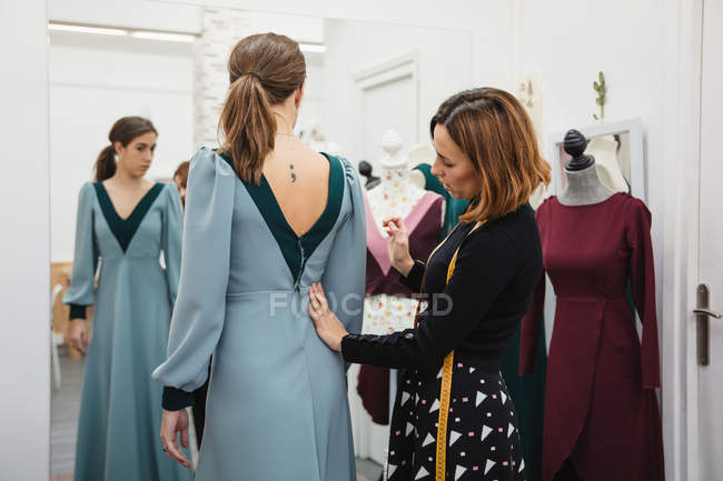 Couturière ajustant robe personnalisée sur le dos du client féminin tout en travaillant dans un atelier professionnel — Photo de stock