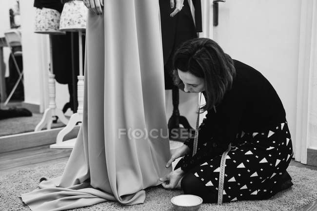 Vestidor de joelhos no tapete e saia de montagem de vestido personalizado enquanto trabalhava em estúdio profissional — Fotografia de Stock
