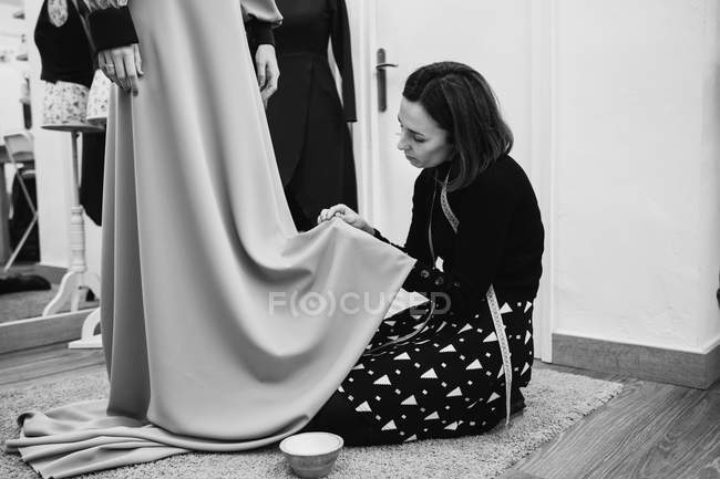 Dressmaker kneeling on carpet and fitting skirt of custom gown while working in professional studio — Stock Photo