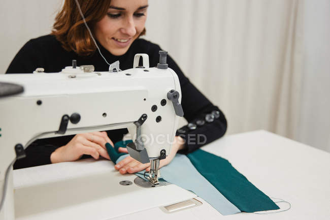 Adult woman sitting at table and making garment part on sewing machine while working in professional studio — Stock Photo