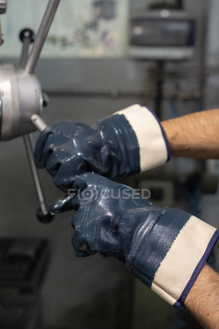 Manos con guantes de maestro masculino irreconocible en el torneado de la válvula de la máquina industrial durante el trabajo en fábrica - foto de stock