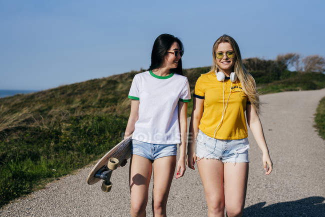 Trendy teen girls with long board in sunshine — Stock Photo