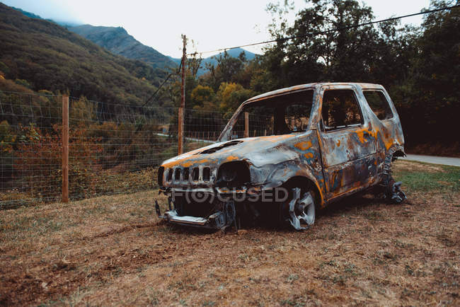 Rusty vehículo roto situado cerca de la cerca contra las montañas en la naturaleza de otoño - foto de stock