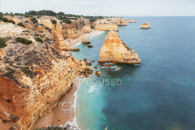 Clean blue sea waving near rough rocky cliffs on cloudless day in Portugal — Stock Photo
