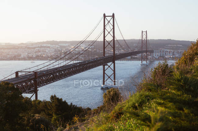 Puente colgante moderno con coches que cruzan el río de la ciudad contra el cielo nocturno sin nubes en Portugal - foto de stock