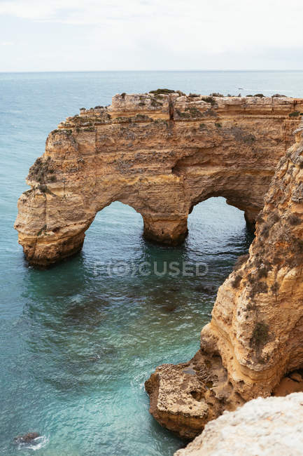 Água do mar limpa ondulação perto de penhasco áspero arqueado em dia calmo em Portugal — Fotografia de Stock