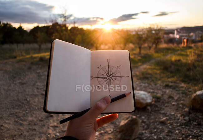Crop traveler drawing compass during sunset — Stock Photo