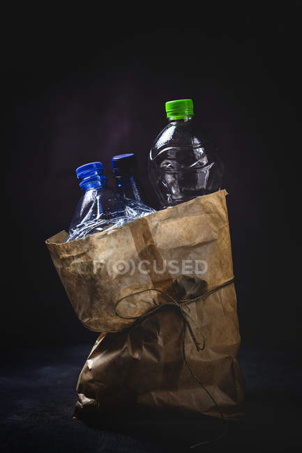 Sacco di carta sporca con bottiglie di plastica scartate poste su sfondo nero — Foto stock