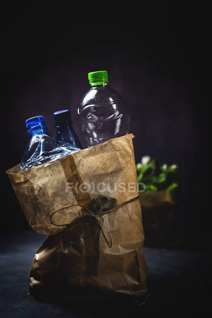 Брудний паперовий мішок з відкинутими пластиковими пляшками, розміщеними на чорному тлі — стокове фото