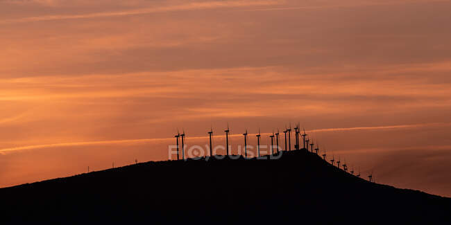 Paisaje industrial que representa la línea de molinos de viento girando cuchillas en las montañas al amanecer con el cielo nublado rosa como fondo - foto de stock