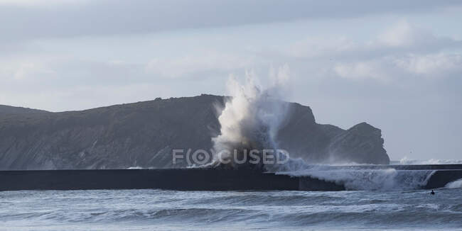 Rough ocean waves crashing on pier with highlands as background during tide — Stock Photo