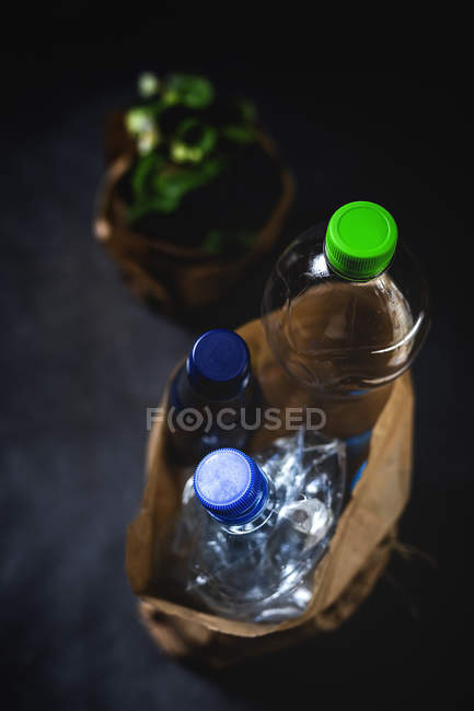 Von oben schmutziger Papiersack mit weggeworfenen Plastikflaschen auf schwarzem Hintergrund — Stockfoto