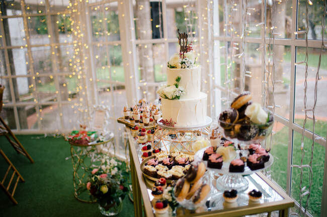 Bolos doces decorados festivos muffins e bolo de flores brancas em stand no restaurante — Fotografia de Stock