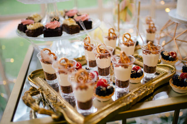 Зверху прикрашені солодкі смачні стрільці з чізкейку на золотому підносі та рожевий квітучий торт на скляній підставці в ресторані — стокове фото