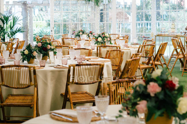 Велика простора кімната зі святковими прикрашеними столами і дерев'яними стільцями під стелею з зеленими рослинами — стокове фото