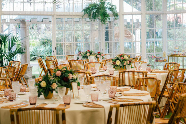 Amplia habitación grande con mesas decoradas festivamente y sillas de madera bajo el techo con plantas verdes - foto de stock