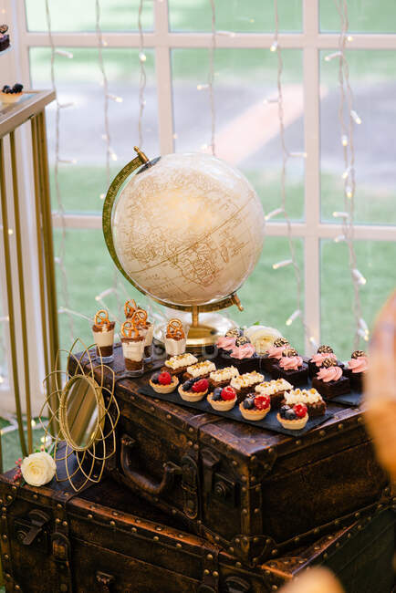Сверху белый и золотой поднос с ягодами и сливочными тортами на черном стенде на декоративных старых чемоданах в ресторане — стоковое фото